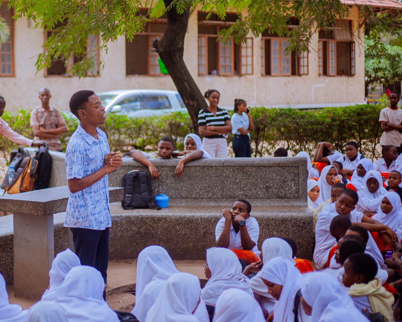 A GROW educator speaks to students gathered under the trees at Jangwani Secondary School